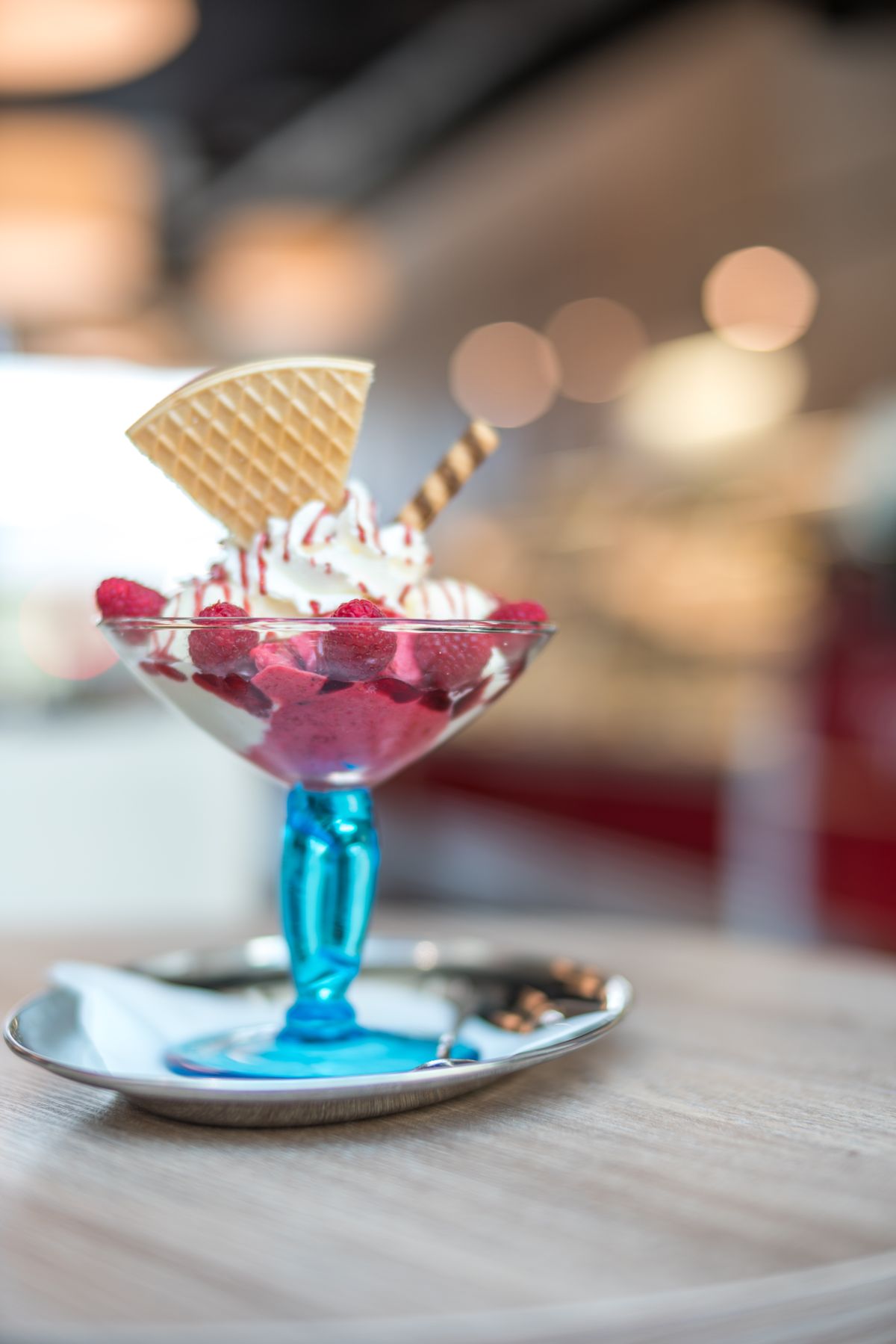 Raspberry sundae with whipped cream and wafer fan in a blue-stemmed glass on a silver tray