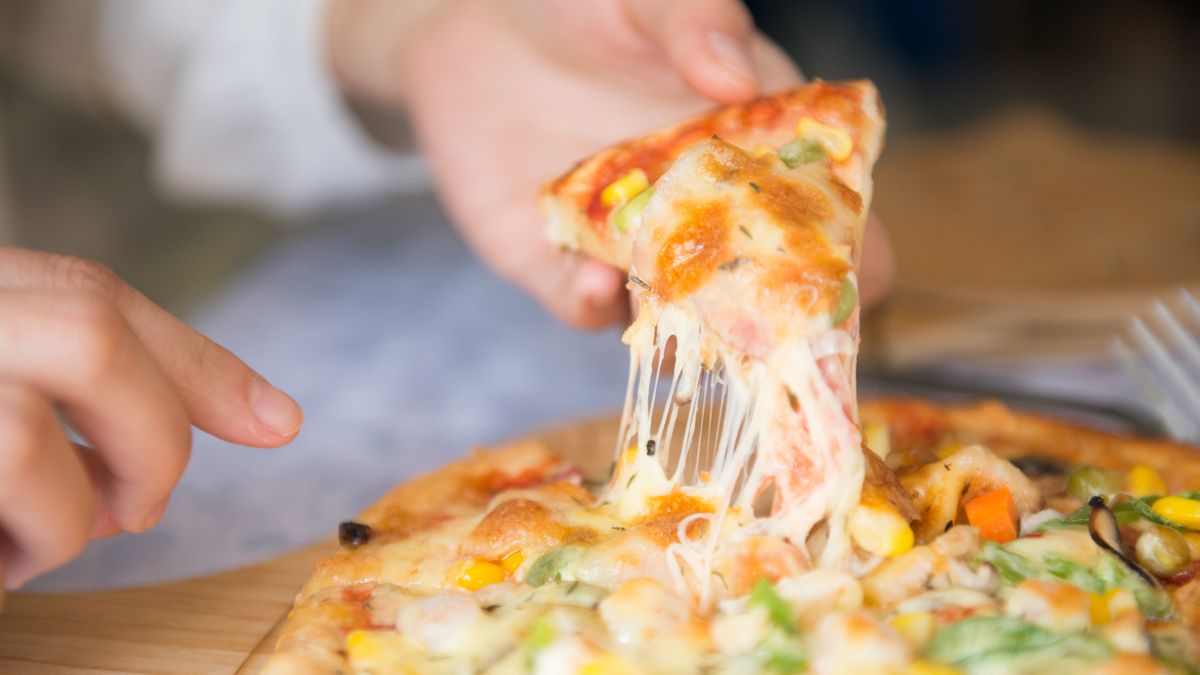 Vegetable pizza slice lifted from the pie showing long stretching melted cheese