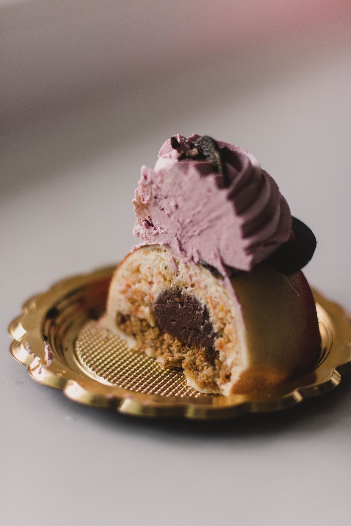Halved dome pastry with lavender frosting swirl and chocolate center on a gold scalloped plate