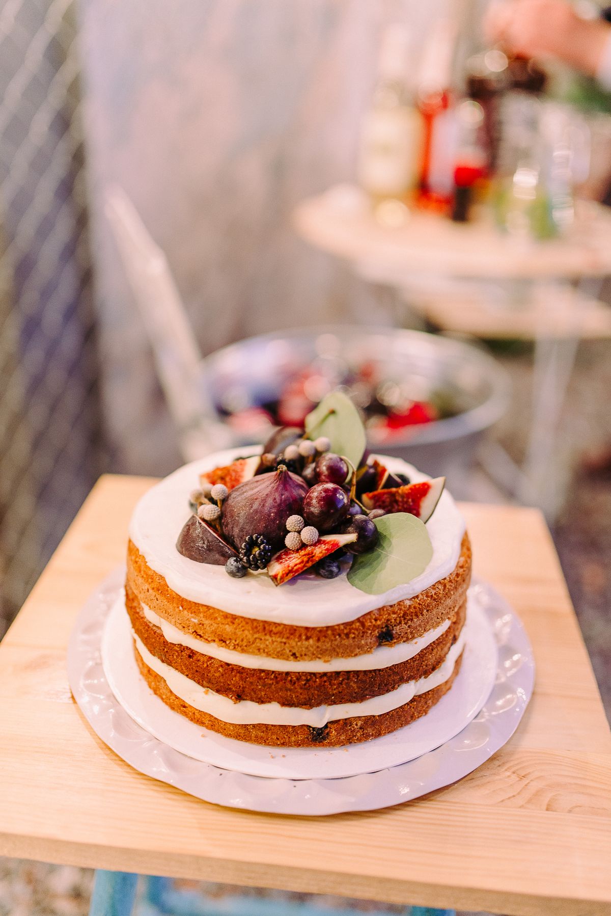 Three-layer naked cake with white frosting topped with fresh figs, berries, and grapes