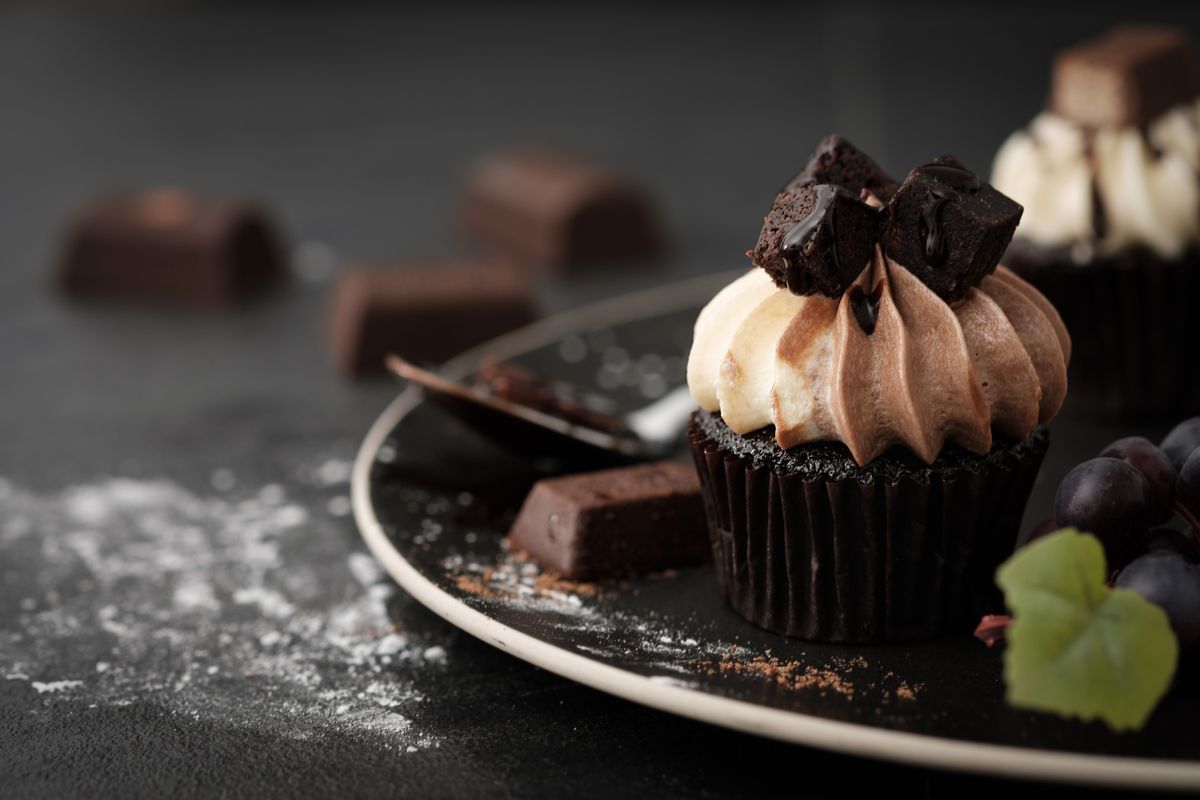 Chocolate cupcake with two-tone frosting swirl, brownie cubes, and chocolate drizzle on a dark plate